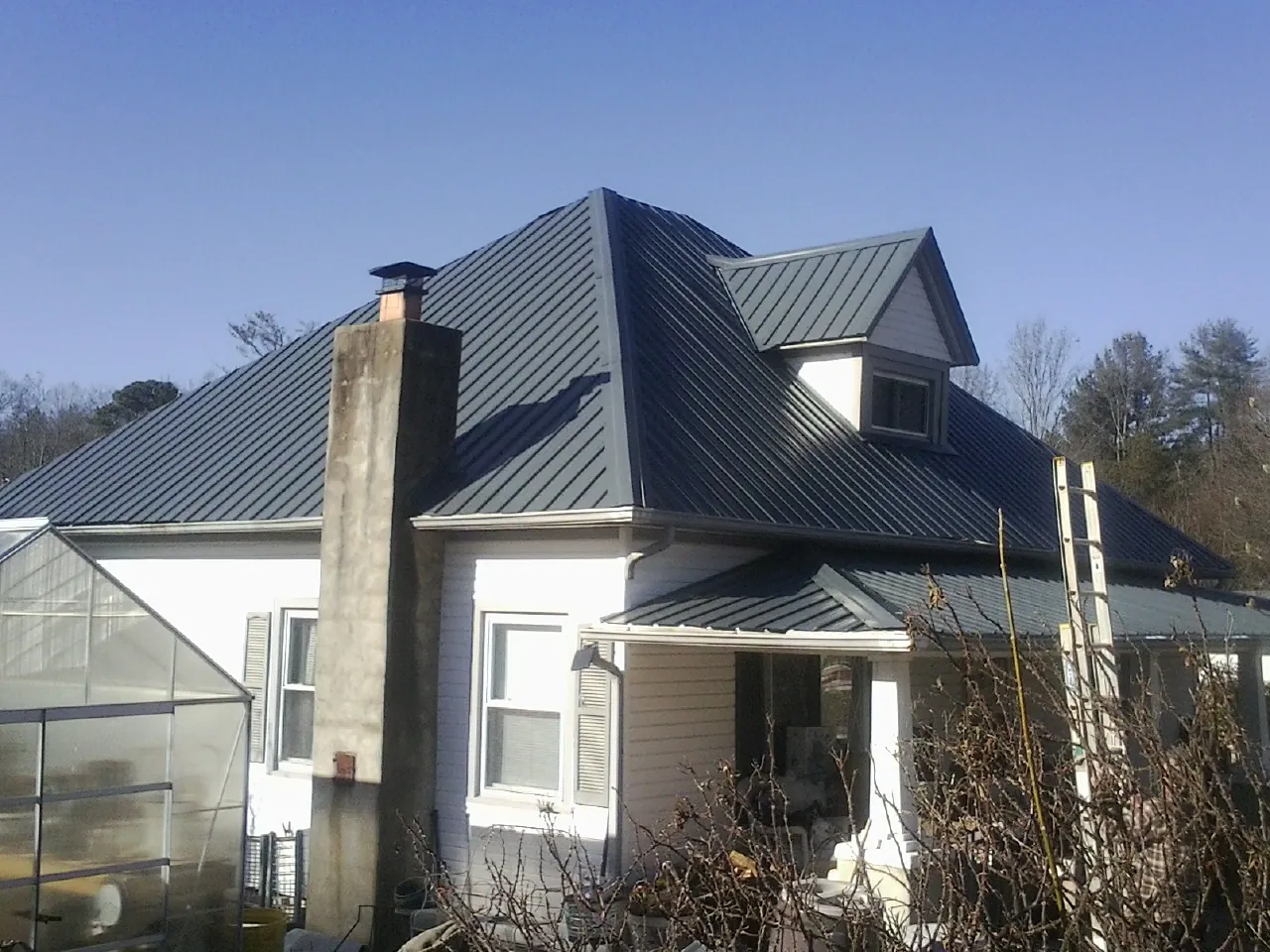 Dark blue standing seam metal roof on a white farmhouse with dormer — Slate & Tile Roof Repair by Roofing Brothers in Caroleen