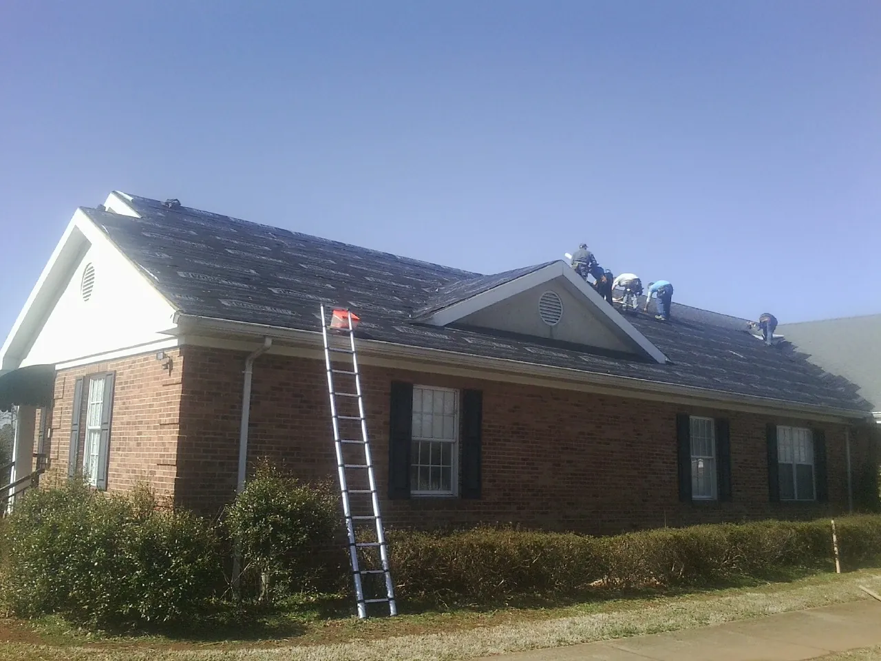 Crew tearing shingles off a brick ranch roof with a ladder set — Emergency Roof Repair work by our crew in Caroleen