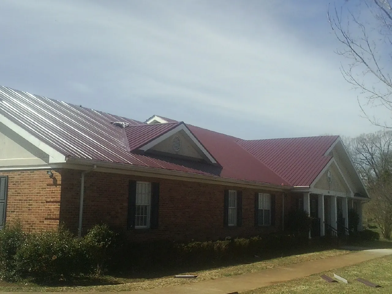 Red metal roof with gabled entries on a long brick building, from a Hail Damage Roof Repair job in Caroleen