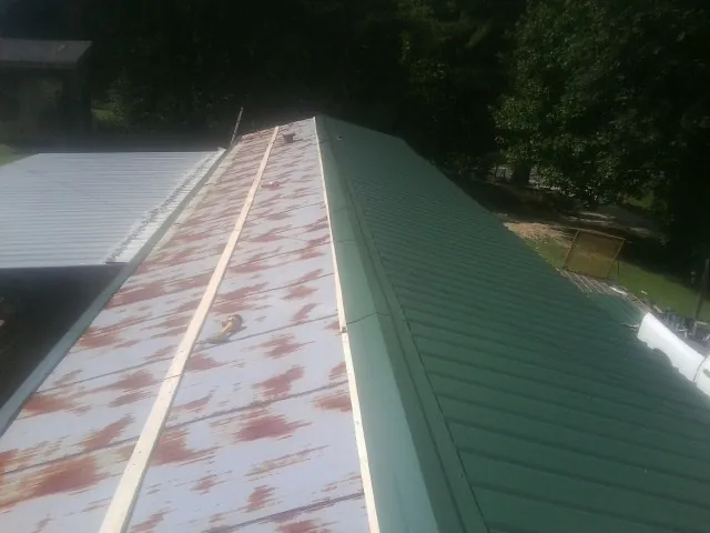 Old rusted panels beside newly installed green metal roofing — Wind Damage Roof Repair by Roofing Brothers in Caroleen