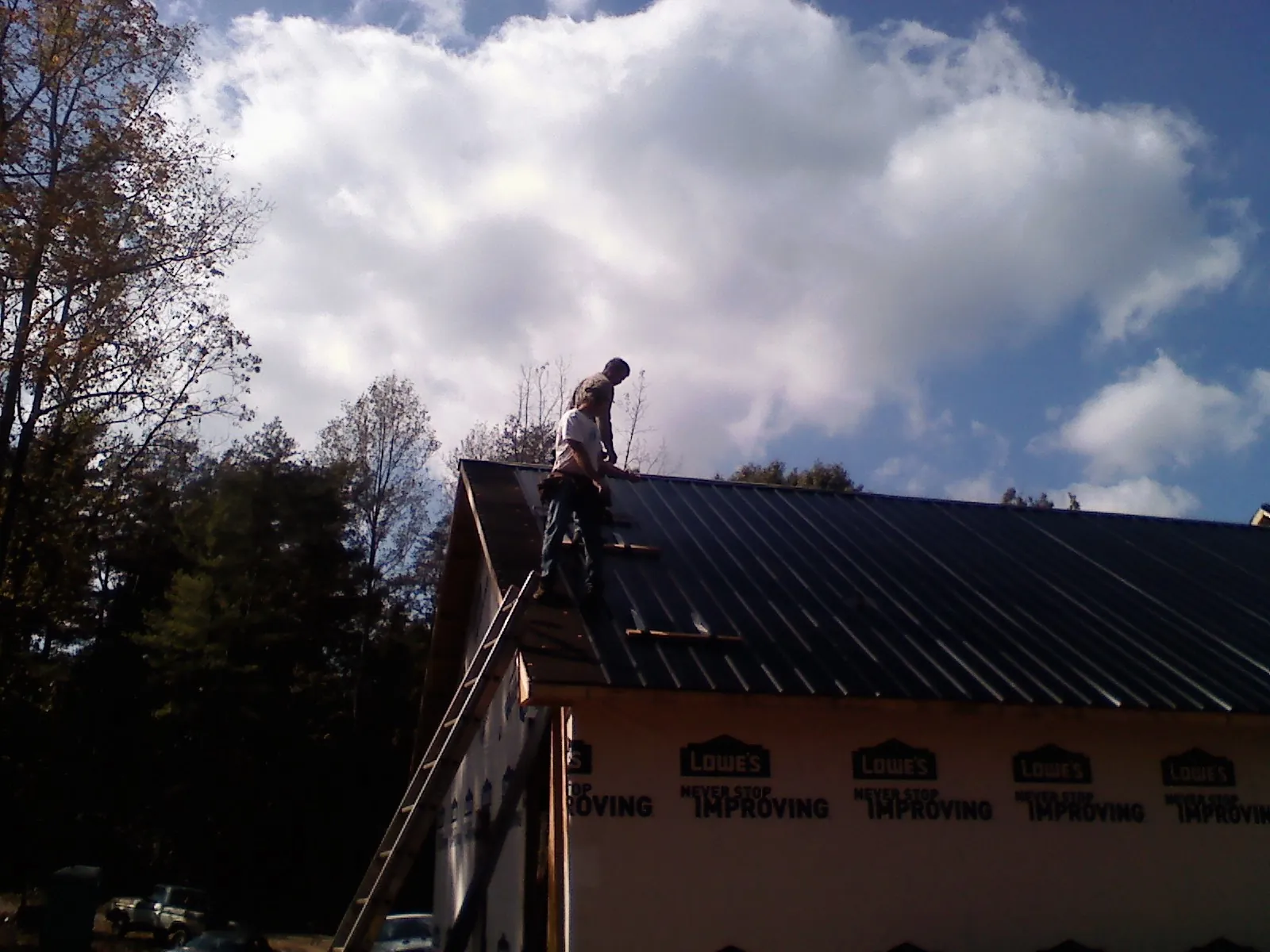 Roofer fastening dark metal panels high against a cloudy sky, from a Roof Inspection job in Caroleen