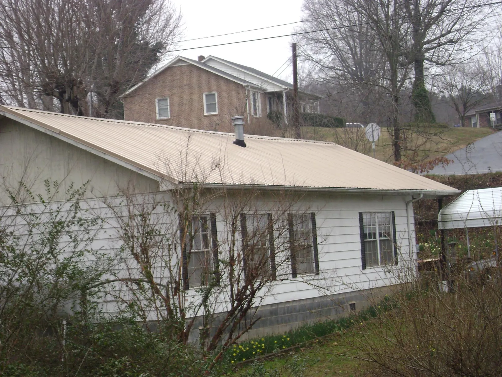 Tan metal roof on a white sided house set into a hillside — Commercial Roofing by Roofing Brothers in Caroleen